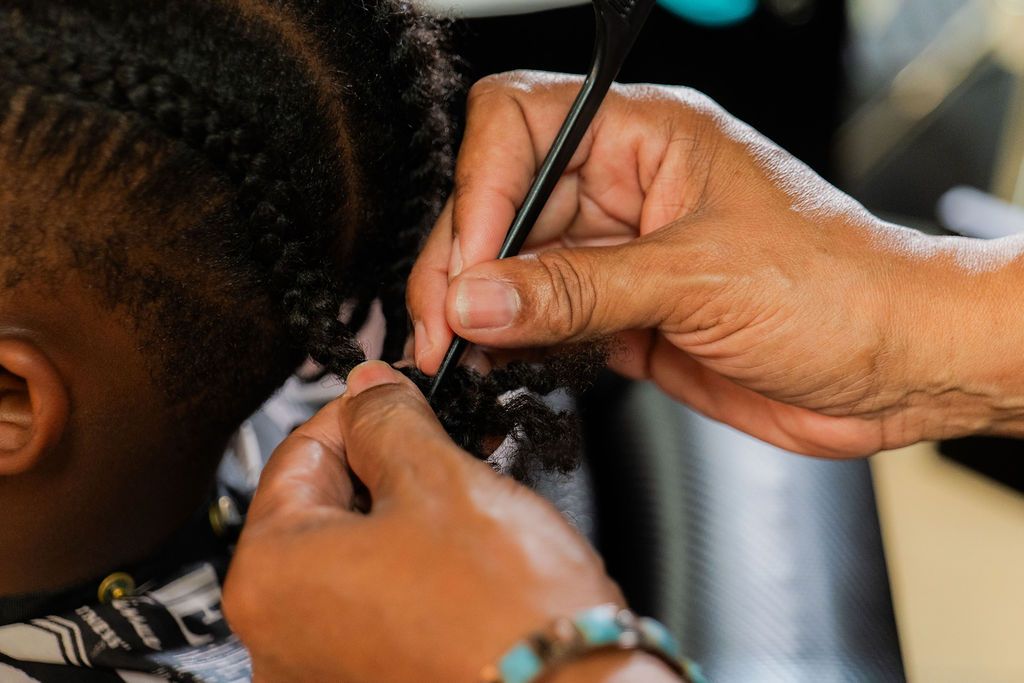 Professional stylist braiding natural textured hair into neat cornrows using a black parting comb.